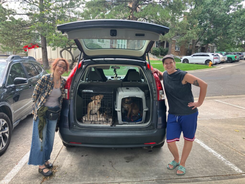 Two volunteers smiling beside an open SUV packed with puppies in transport crates